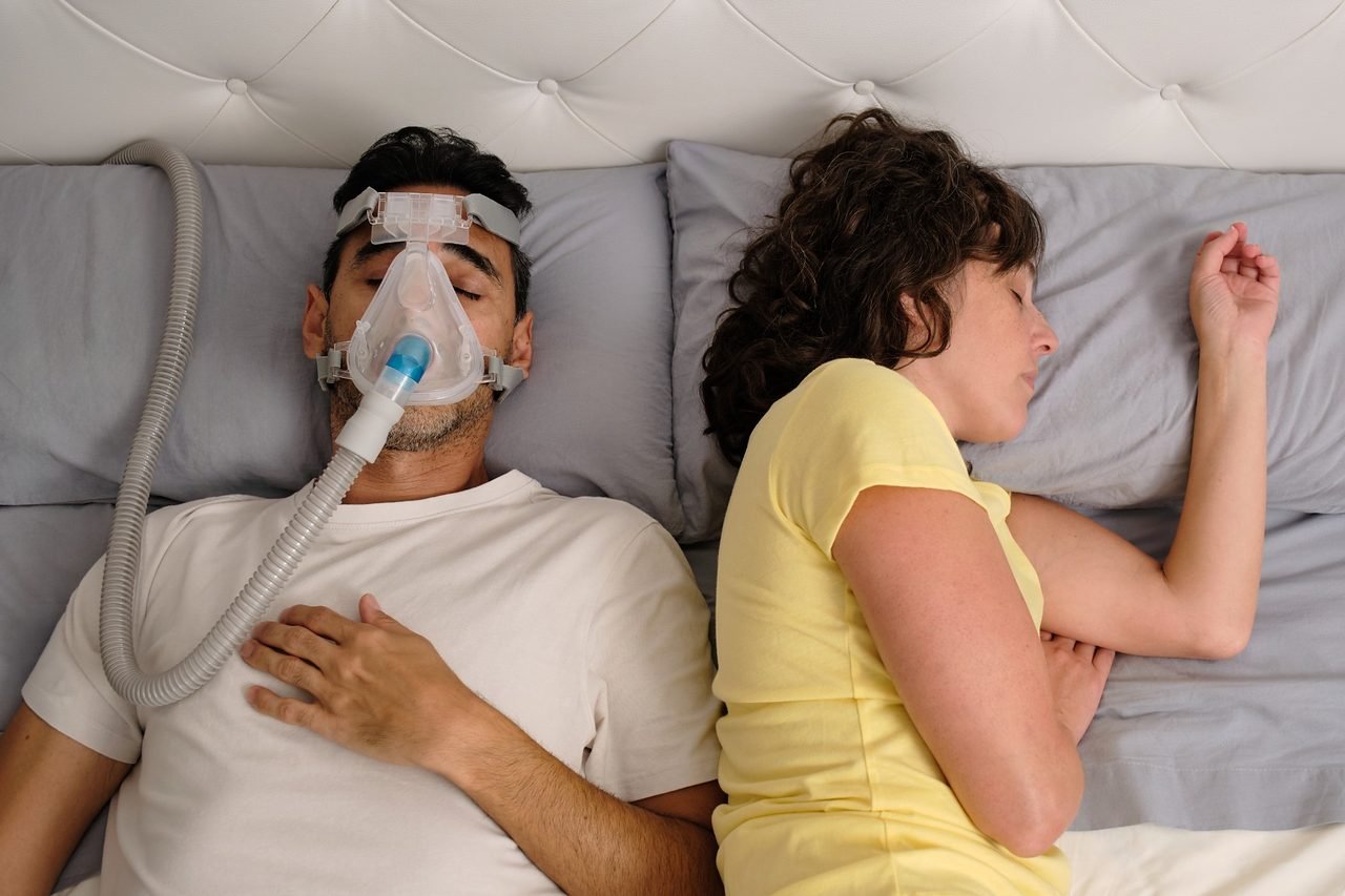 Man sleeping on his back wearing a CPAP mask beside his partner