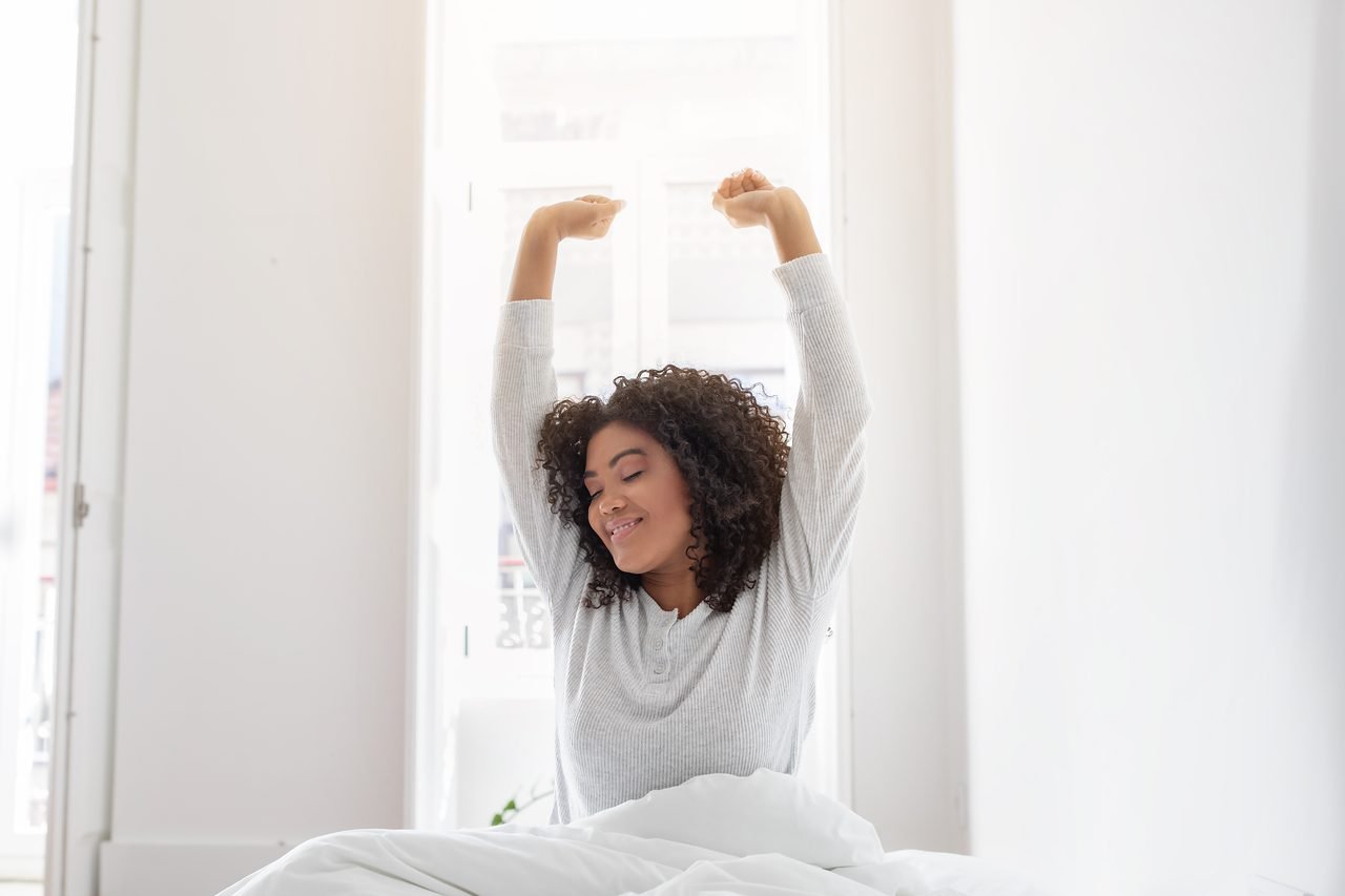 Woman sitting up in bed and stretching her arms overhead after waking up