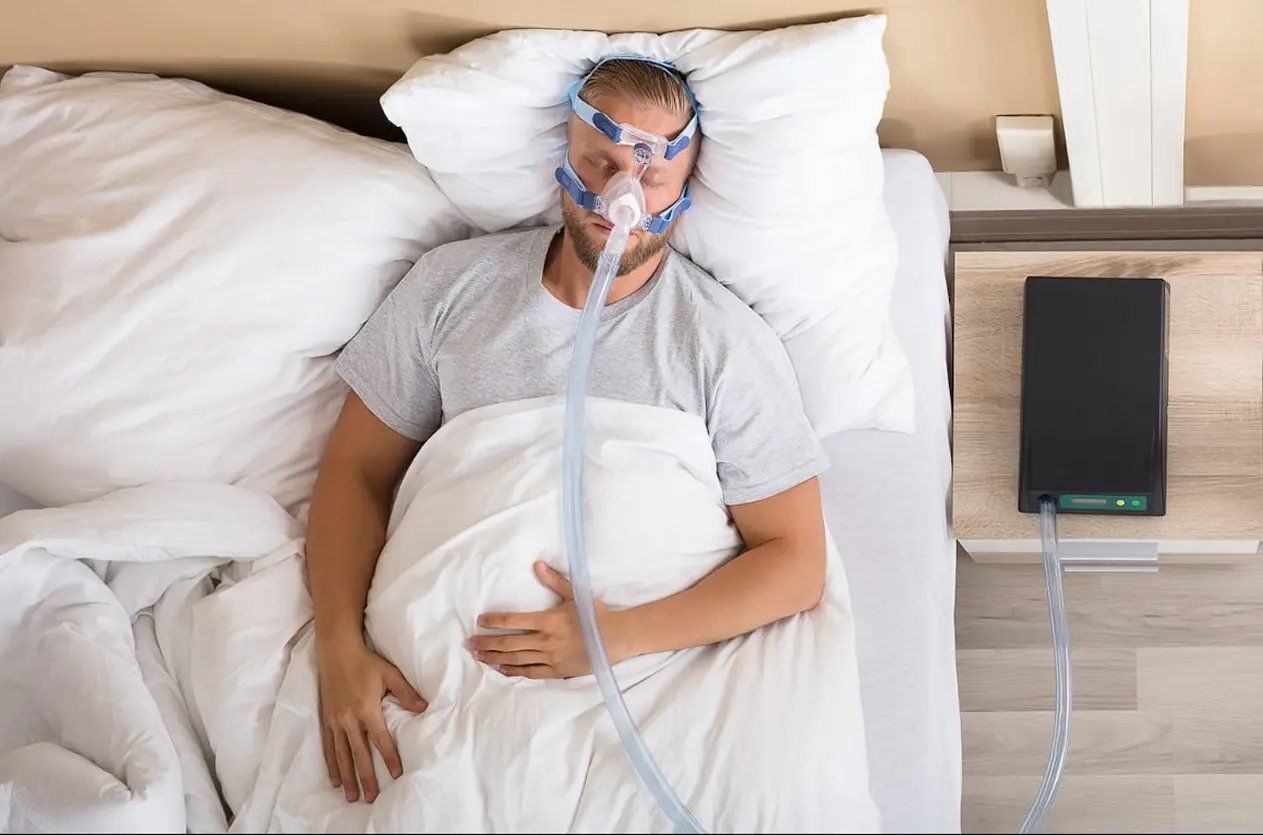 Man sleeping in bed wearing a bulky CPAP mask and straps, illustrating traditional sleep apnea treatment