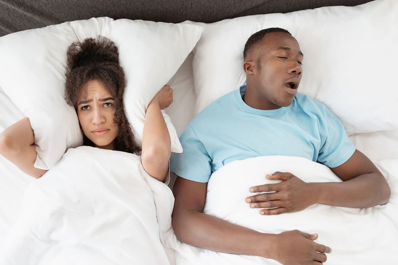 Woman covering her ears with a pillow while her partner snores in bed