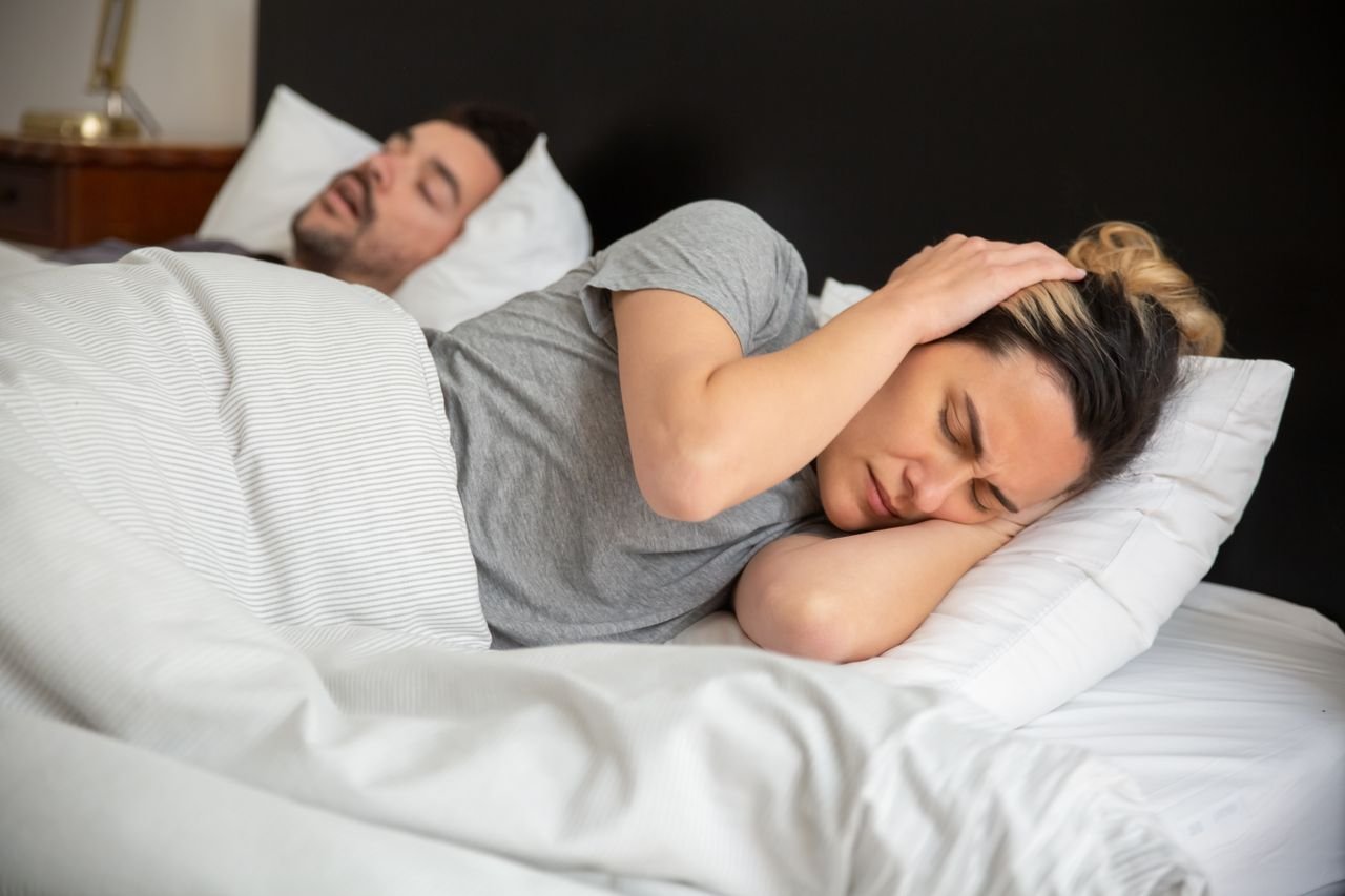 A man snoring in bed while his partner covers her ears