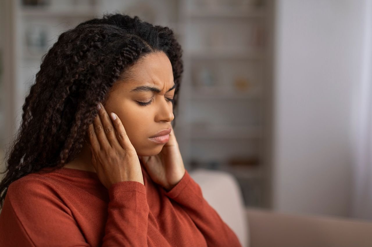 Woman pressing her hands to her jaw and ears in discomfort