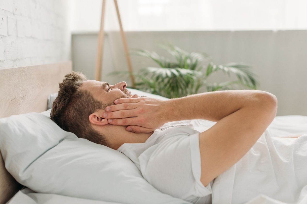 Man lying in bed holding his jaw in pain