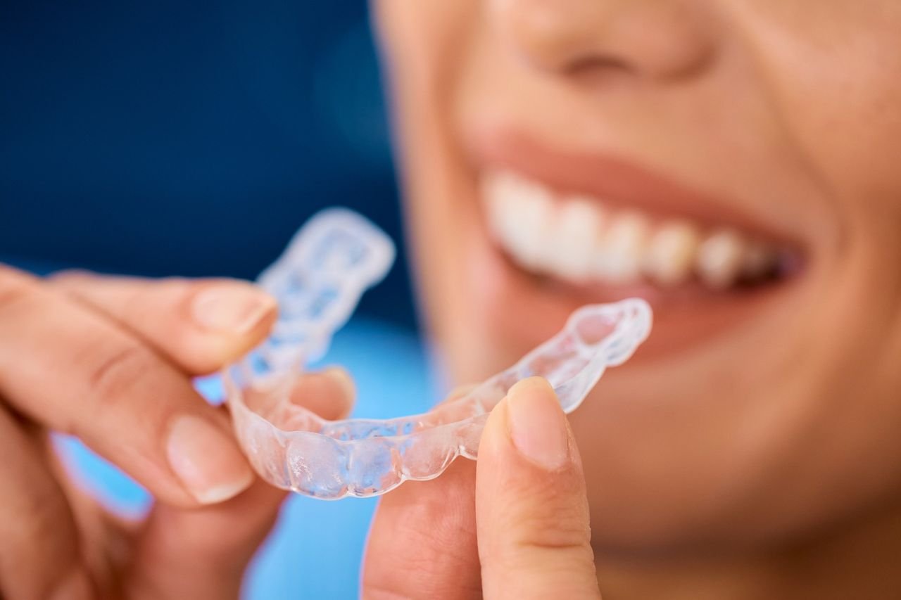 Smiling patient holding a clear aligner
