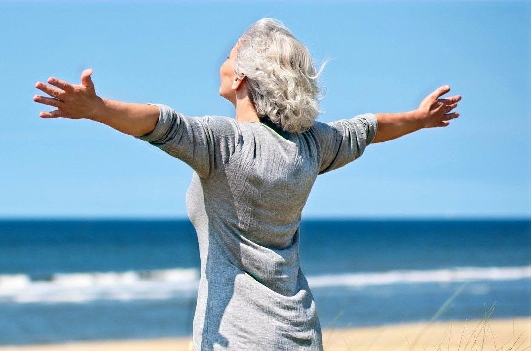 Woman breathing freely with open arms by the ocean